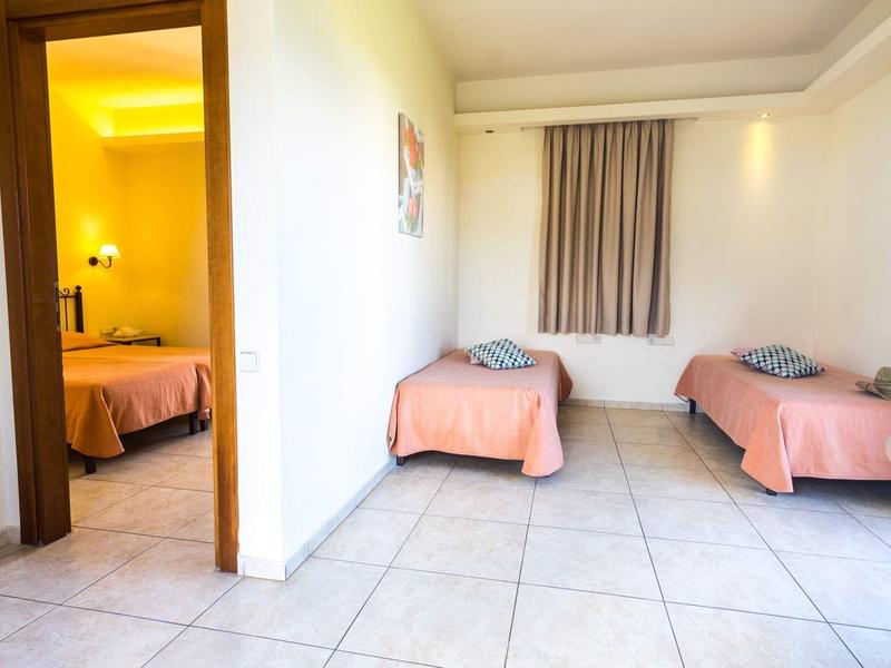 Světložlutý pokoj se dvěma jednoduchými jednolůžky a dlažbou vedle místnosti s dalším lůžkem.