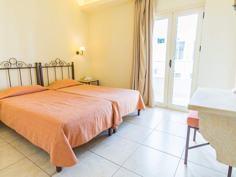 Světelný hotelový pokoj se dvěma jednolůžky, oranžovými přikrývkami a balkonem