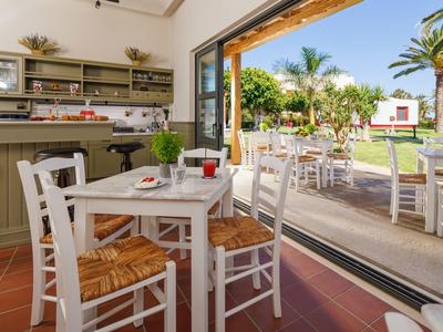 Interno accogliente di un caffè con sedie e tavoli bianchi che si apre su una terrazza soleggiata con palme.