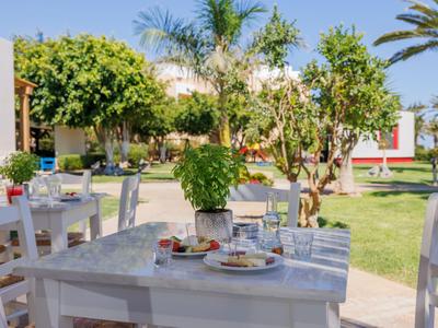 Tavolo apparecchiato con cibo e bevande su una terrazza accanto a un giardino con alberi.