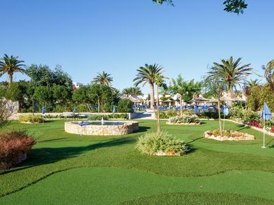 Prato verde con palme e ombrelloni in un giardino soleggiato dell'hotel