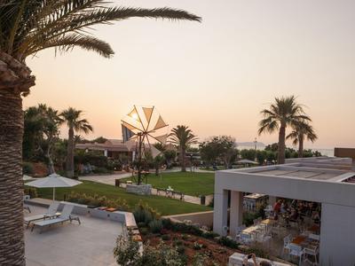 Tramonto in un giardino di un hotel con mulino a vento, palme e sedie a sdraio.