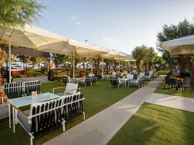 Area ristorante all'aperto con tavoli, sedie e ombrelloni su prato verde.