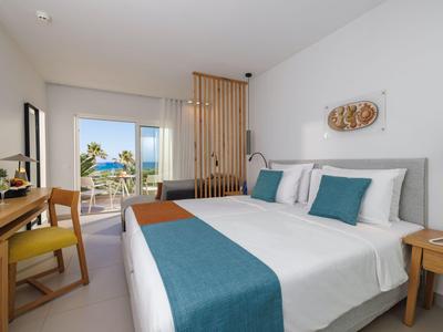 Camera d'hotel luminosa con letto matrimoniale, copriletto blu e terrazza con vista sul mare