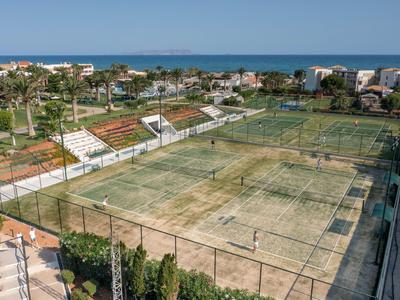 Campi da tennis con reti e vegetazione circostante davanti a una città costiera e al mare sullo sfondo.