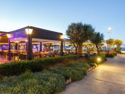 Vista serale di un ristorante all'aperto illuminato con alberi e percorso vicino al mare.