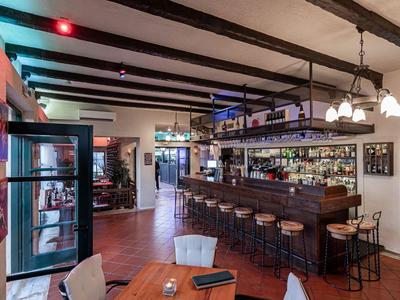 Bar dell'hotel moderna con bancone in legno, sgabelli e area pranzo accogliente, illuminata da luce calda.