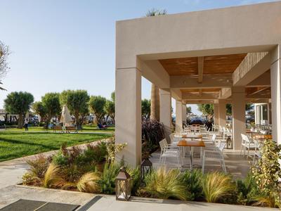 Area aperta di un hotel con sedie, tavoli e vista su un giardino ben curato alla luce del giorno.