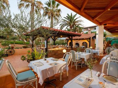 Terrazza coperta di un ristorante con tavoli apparecchiati e vista su palme e giardino.