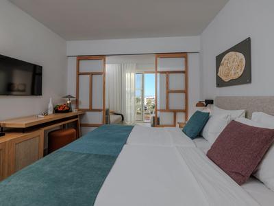 Camera d'hotel moderna con grande letto matrimoniale, TV e vista sul balcone attraverso porte scorrevoli in vetro.