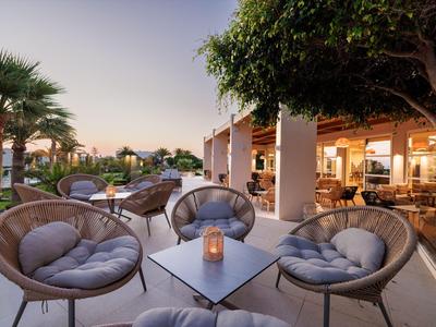 Área exterior acogedora de un hotel con sillones y mesa al atardecer.
