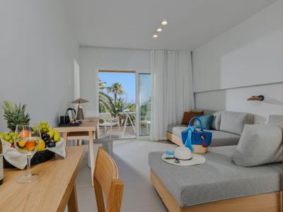 Habitación de hotel moderna con área de estar, escritorio y balcón con vista al mar.