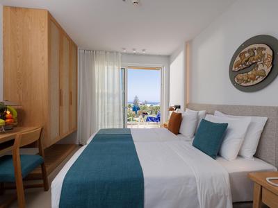 Habitación de hotel luminosa con cama doble, muebles de madera y vista al mar a través de grandes ventanas.