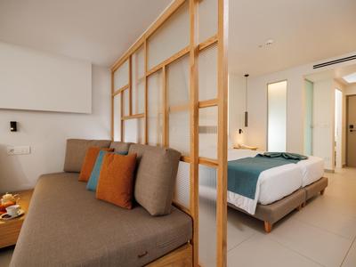 Habitación de hotel moderna con sofá, cojines coloridos y una cama acogedora.