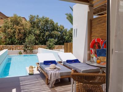 Área exterior moderna con piscina, tumbonas y muebles de madera junto a una habitación de hotel.