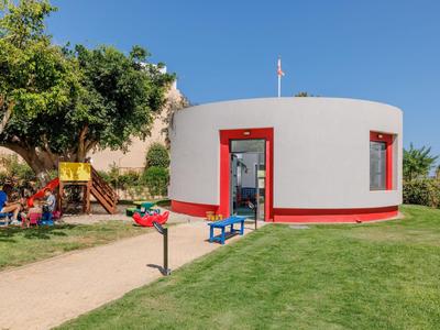 Casa de vacaciones moderna y redonda con acentos rojos, rodeada de áreas verdes y parque infantil.