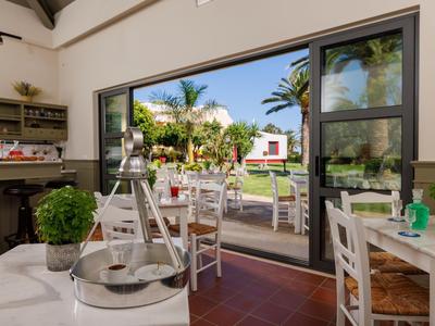 Restaurante luminoso con vistas a un jardín con piscina y palmeras.