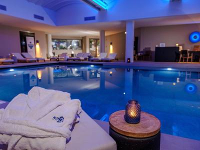 Piscina cubierta con agua tranquila, batas blancas y luz suave en un hotel.