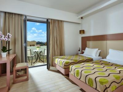 Chambre d'hôtel avec deux lits simples, balcon avec table et chaises, sol clair et vue sur la verdure.