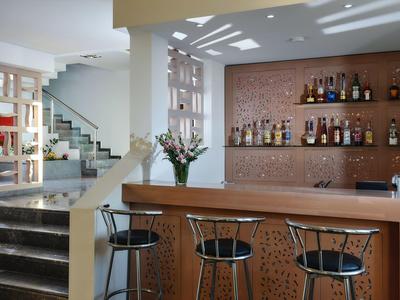 Espace bar d'hôtel moderne avec comptoir en bois, tabourets de bar et étagères décoratives dans des tons clairs.