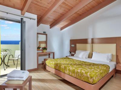 Chambre d'hôtel lumineuse avec plafond à poutres en bois, lit double et balcon avec vue sur la mer.