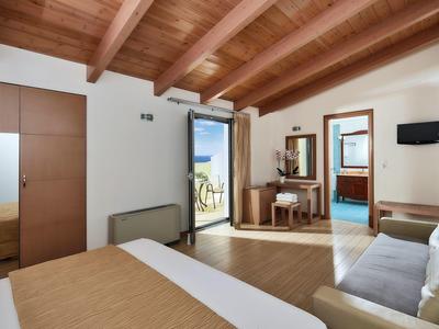 Chambre d'hôtel lumineuse avec plafond à poutres en bois et vue sur balcon et mer.