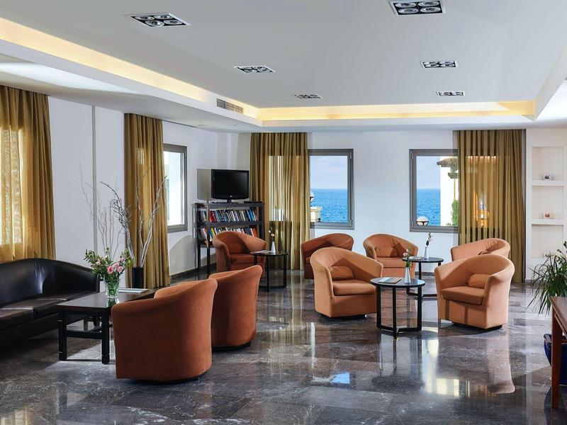 Salon d'hôtel lumineux avec fauteuils confortables, grandes fenêtres et vue sur la mer.