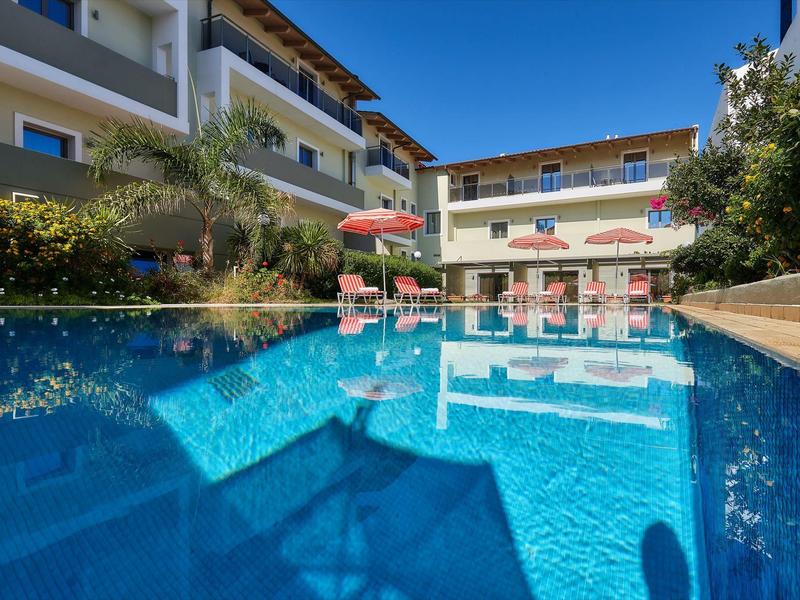 Piscine d'hôtel moderne avec chaises longues bleues et parasols rouges sous un ciel ensoleillé.
