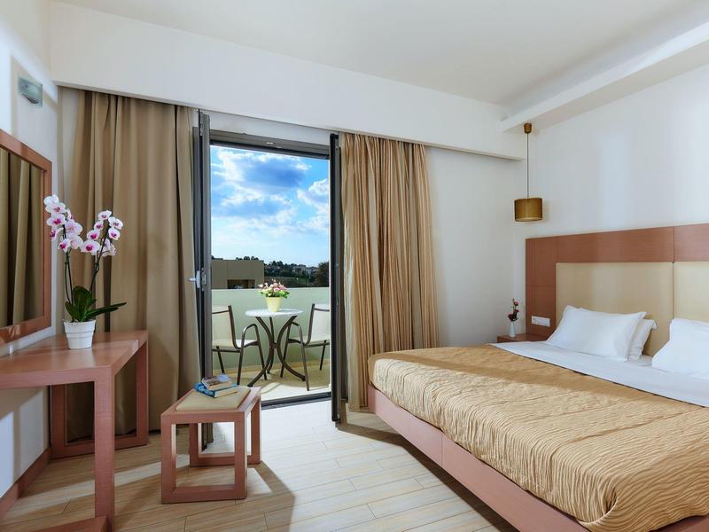 Chambre d'hôtel lumineuse avec lit double, table avec chaises et vue sur balcon et paysage.
