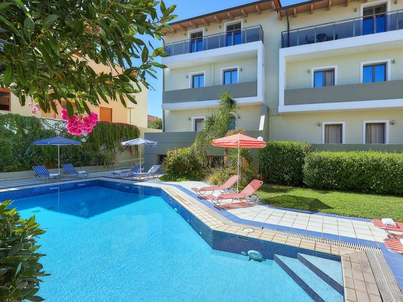 Piscine d'hôtel moderne avec transats, parasol et plantes en fleurs dans le jardin.