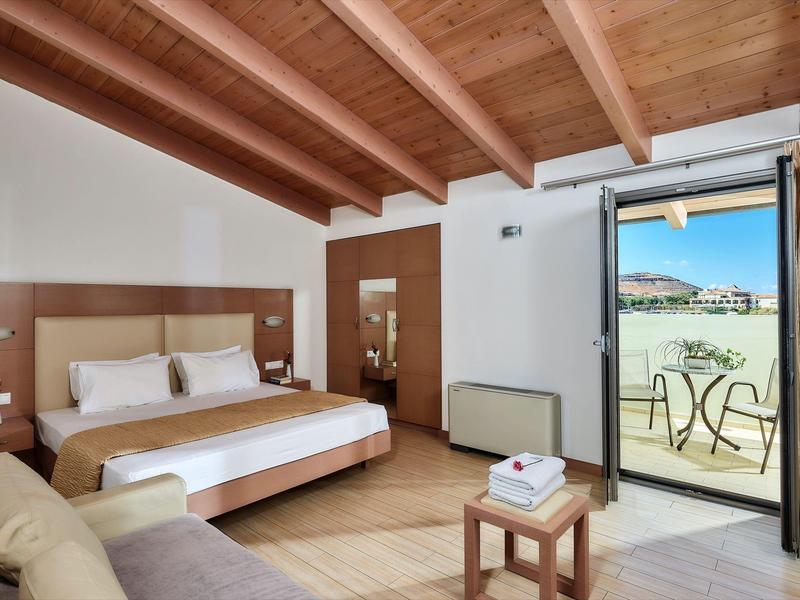 Chambre d'hôtel lumineuse avec plafond à poutres en bois, lit double et balcon donnant sur la mer.