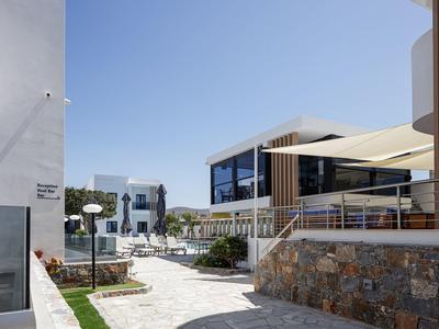 Modern hotel complex with white building, glass facade, and outdoor seating area under sunshades.