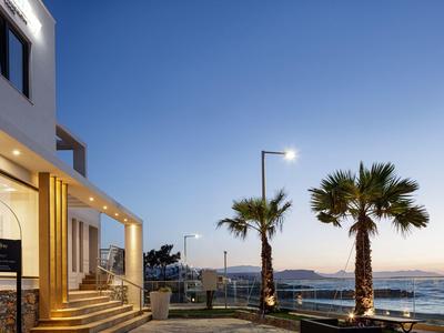 Modern hotel entrance at sunset with palm trees and sea view.
