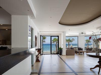 Bright hotel lobby area with sea view through large windows and a terrace.