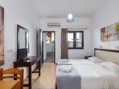 Ein helles Hotelzimmer mit Doppelbett, Fernseher und Tür zu einem Balkon oder außenbereich.