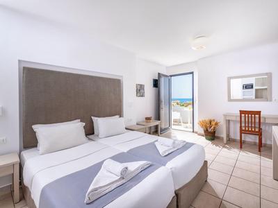 Světý hotelový pokoj se dvěma postelemi, psacím stolem a balkonem s výhledem na moře.