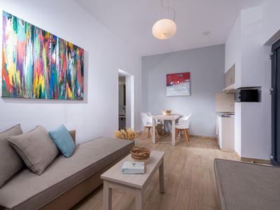 Modern living space with sofa, colorful painting, dining table, and open kitchen in bright room.