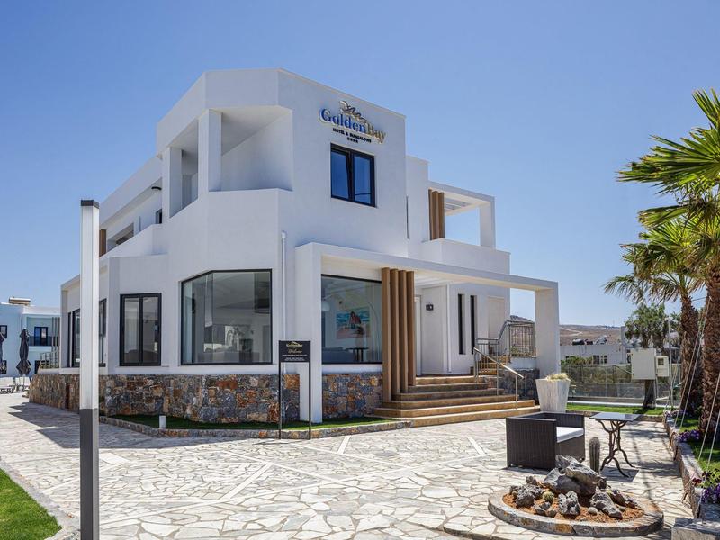 Modern white hotel building with terrace and palm trees under a blue sky.