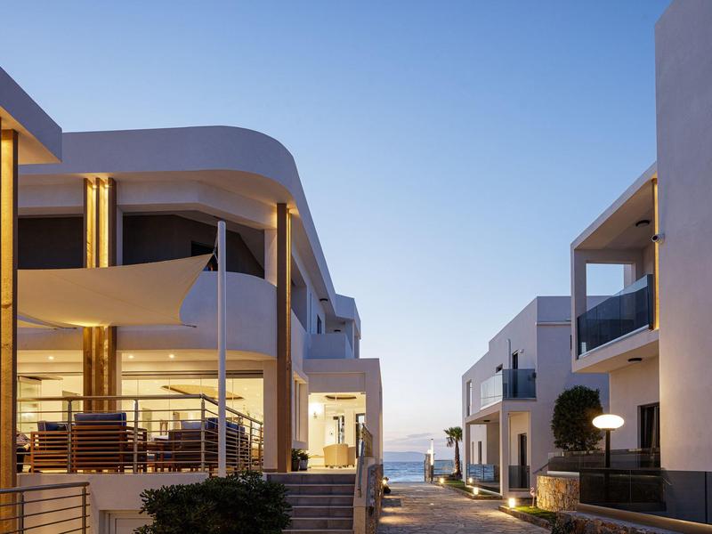 Modern hotel complex at sunset with lit balconies and a pathway in between.