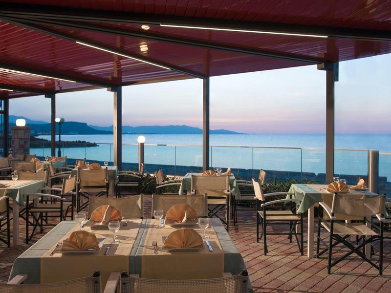 Outdoor restaurant with set tables under a covered area overlooking the sea.