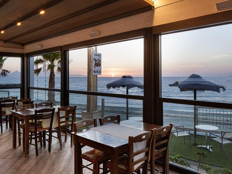 Restaurant with wooden tables and chairs overlooking the sea at sunset.