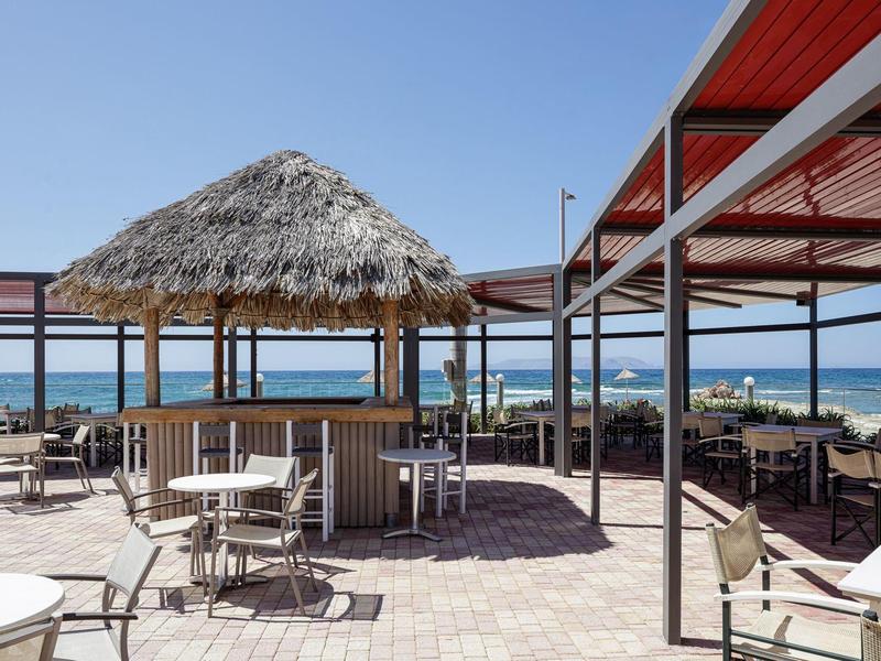 Beach bar with thatched roof and seating, view of the sea and clear sky.
