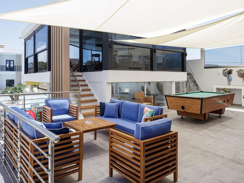 Modern outdoor area with wooden sofas, pool table, and sunshade on a hotel terrace.