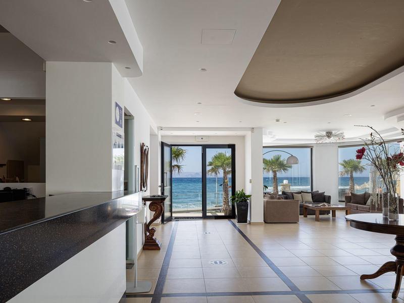 Bright hotel lobby area with sea view through large windows and a terrace.