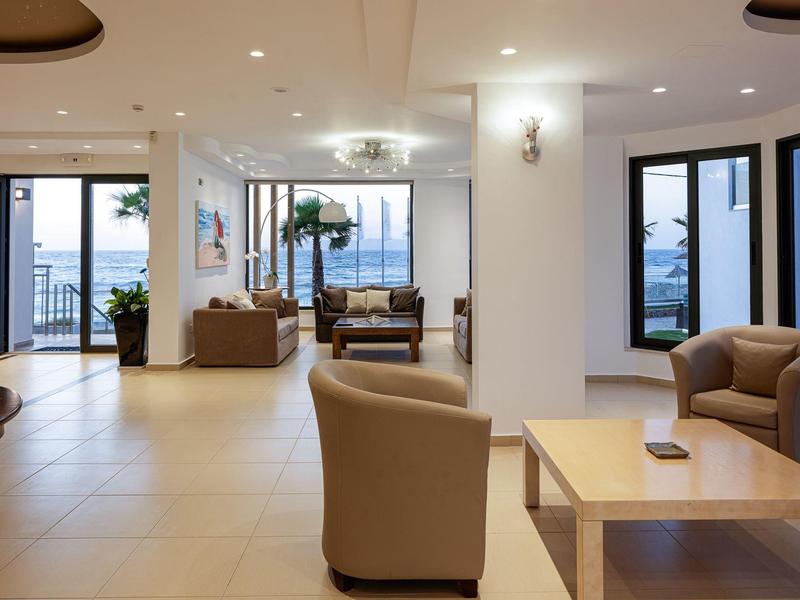 Bright hotel lounge with seating area and large windows overlooking the sea.