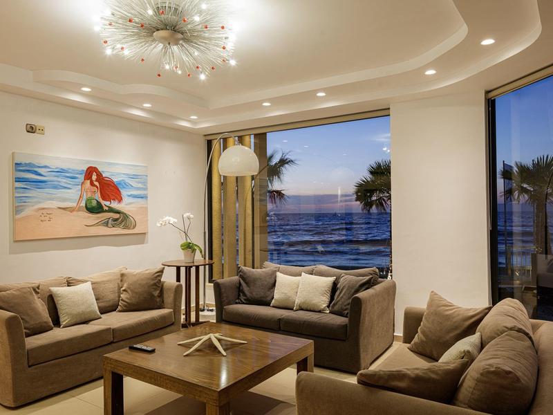 Modern living room with large windows and sea view at sunset.