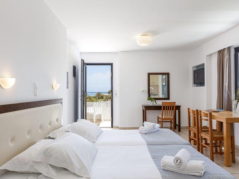 Bright hotel room with two beds, wooden chairs, and sea view from the balcony.