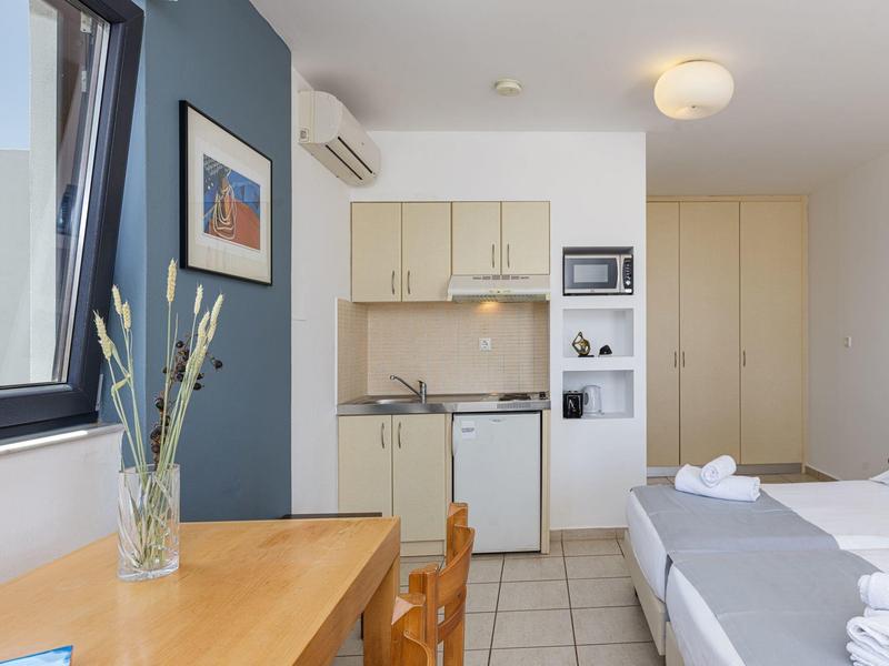 Modern hotel room with kitchenette, large bed, and desk with a vase.
