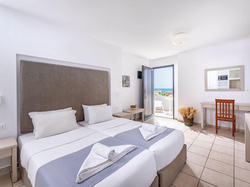 Modern hotel room with two single beds, desk, and sea view through glass doors.