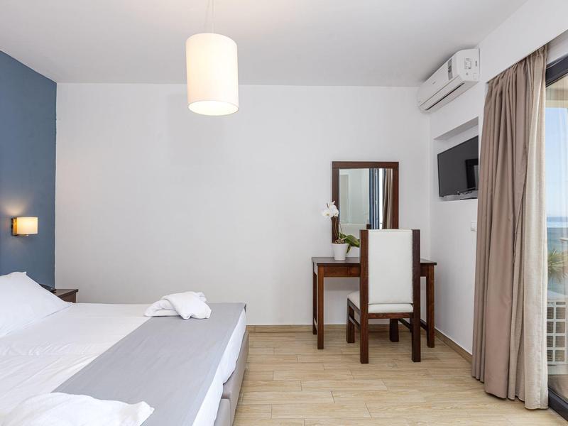 Bright hotel room with double bed, desk, mirror, and balcony with curtains.